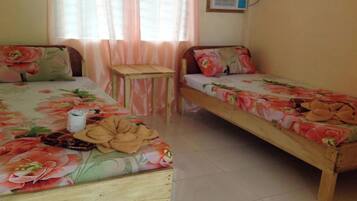 A room with two wooden beds, each with floral bedding. There is a small wooden table between the beds.