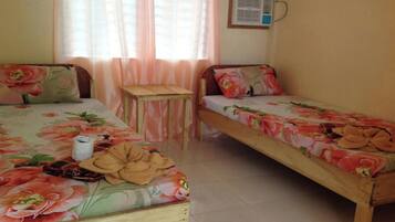 A bedroom with two single beds, a small wooden table, and a window with sheer curtains.