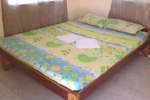 Una cama con ropa de cama floral y dos almohadas, un cabecero de madera y una pared lisa.
