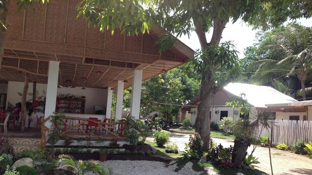 A covered outdoor seating area with tables and chairs, surrounded by potted plants and a gravel path. - Casa Paliton Siquijor Near Beach By Zuzu (San Juan)