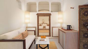 A compact hotel room with a sofa, a small table with a magazine, a coffee maker, and a decorative cabinet.