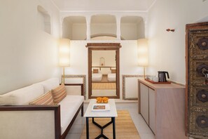 A compact hotel room with a sofa, a small table with a magazine, a coffee maker, and a decorative cabinet. - Gulab Haveli - Ihcl Seleqtions, Mandawa (Jhunjhunu)