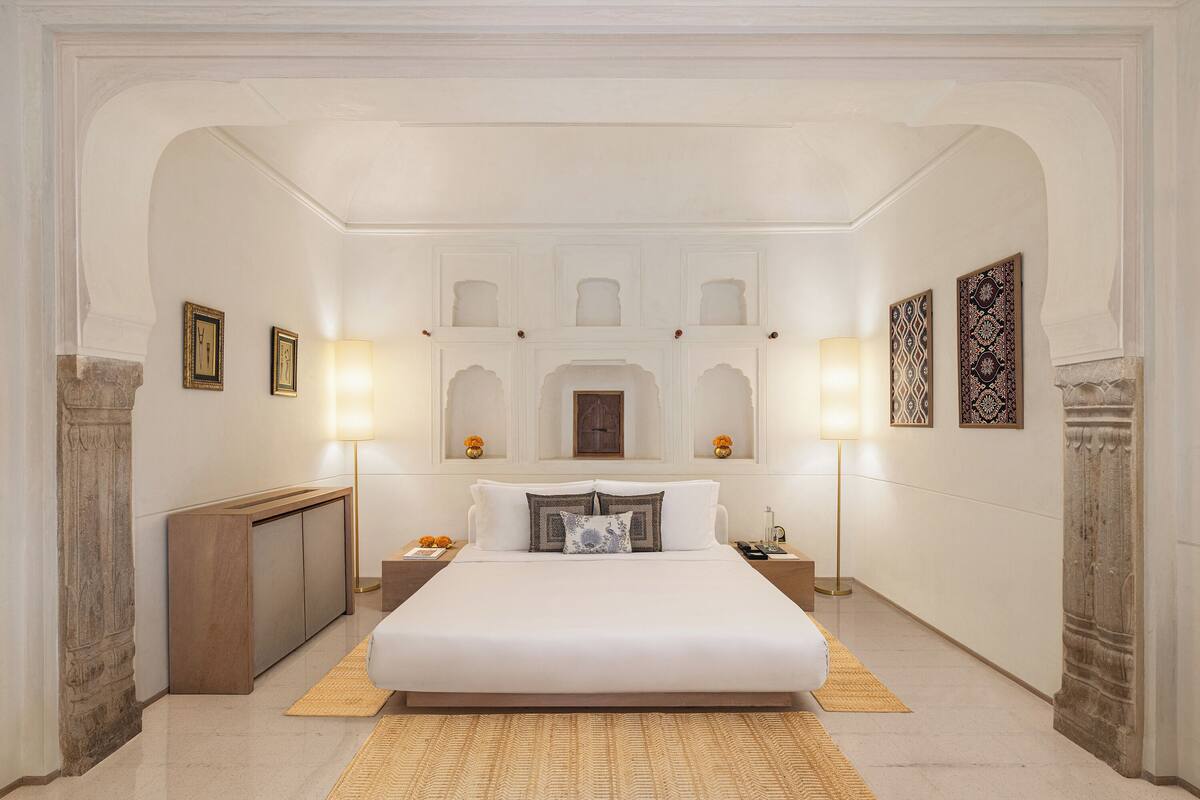 A spacious bedroom with a large bed, a wooden bench, and a nightstand with a lamp.