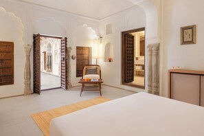 A room with a bed, a chair, and a desk. There are doors leading to other rooms. - Gulab Haveli - Ihcl Seleqtions, Mandawa (Jhunjhunu)