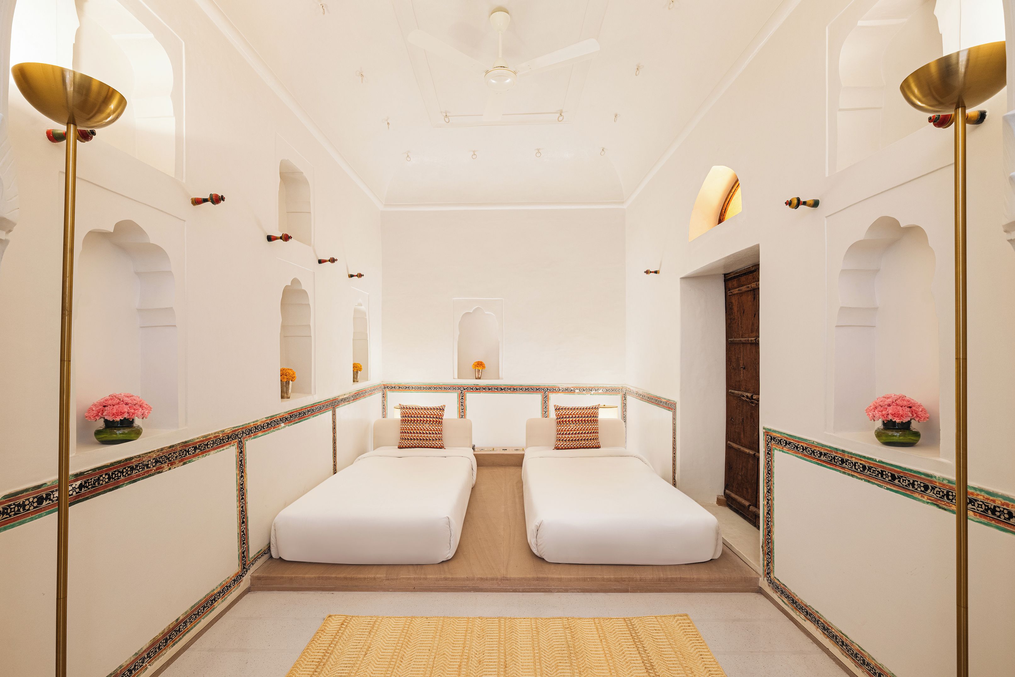 A hotel room with two single beds, a wooden floor, a decorative border, and a ceiling fan.