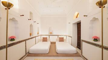 A hotel room with two single beds, a wooden floor, a decorative border, and a ceiling fan.