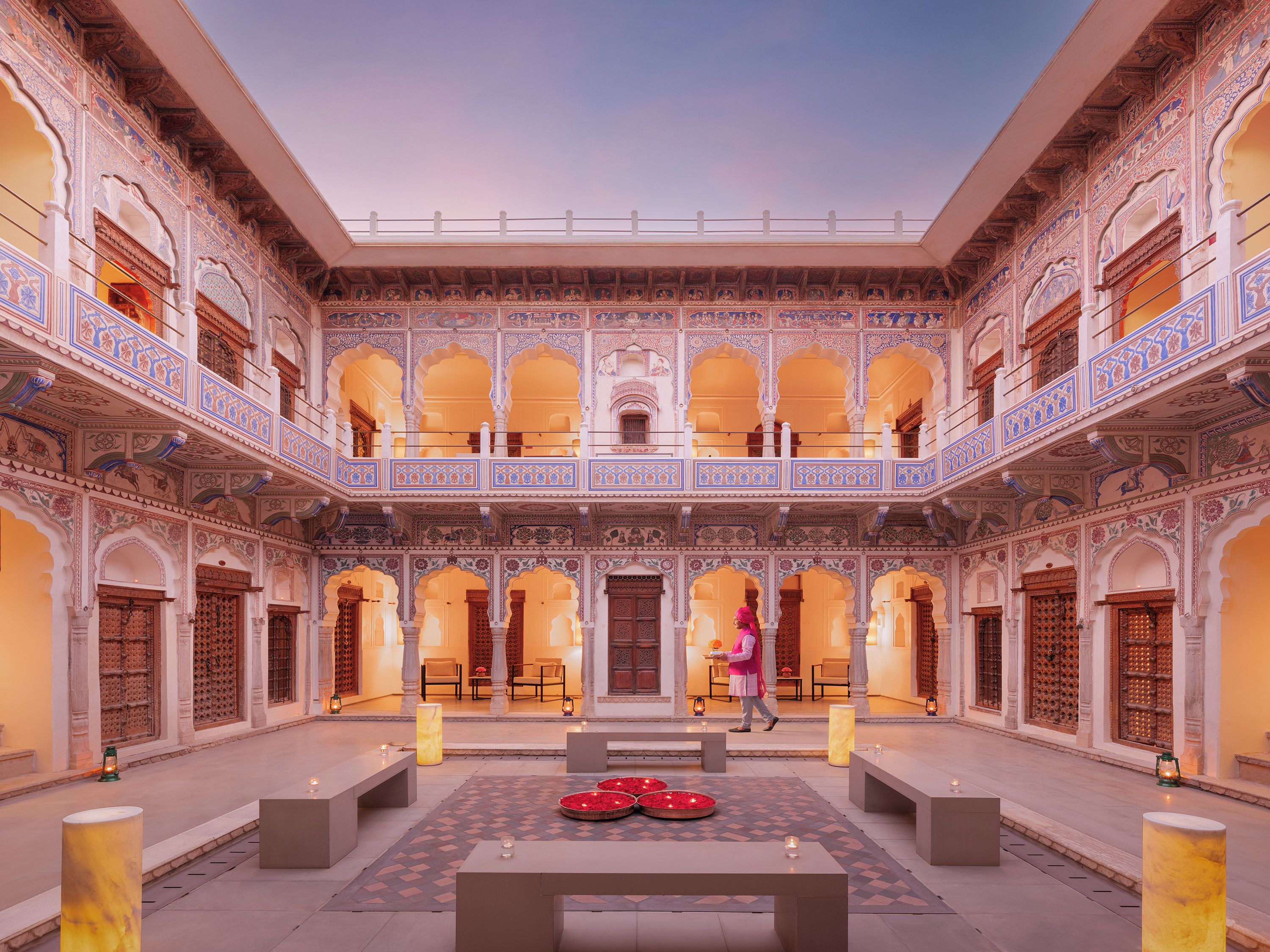 A courtyard with ornate architecture, a central seating area, and a person walking.