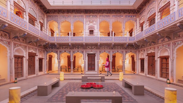 Un cortile con architettura decorata, un'area salotto centrale e una persona che cammina.