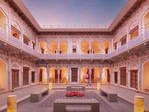 A courtyard with ornate architecture, a central seating area, and a person walking. - Gulab Haveli - Ihcl Seleqtions, Mandawa (Jhunjhunu)
