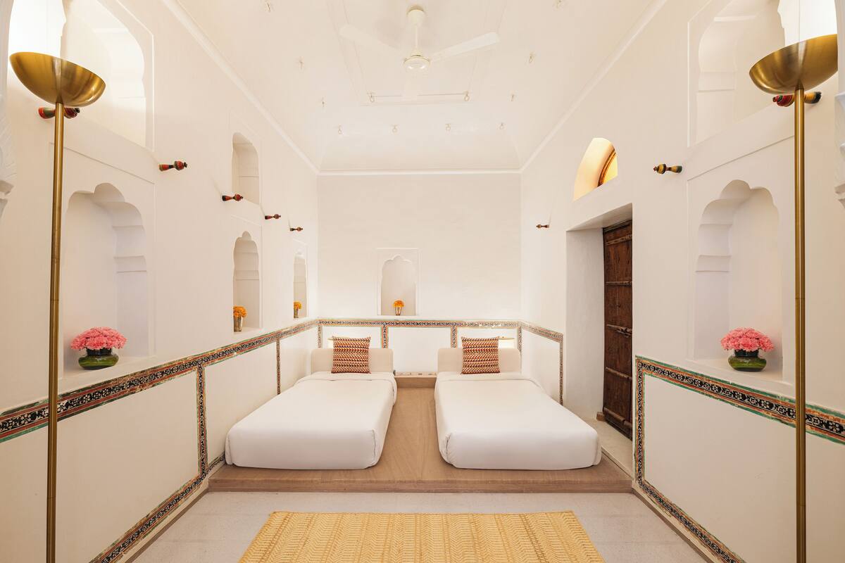 A hotel room with two single beds, a ceiling fan, and decorative wall sconces.