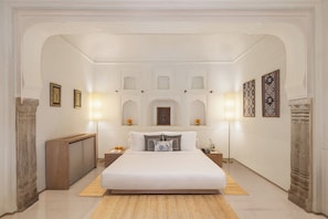 A spacious bedroom with a large bed, a wooden bench, and a nightstand with a lamp. - Gulab Haveli - Ihcl Seleqtions, Mandawa (Jhunjhunu)