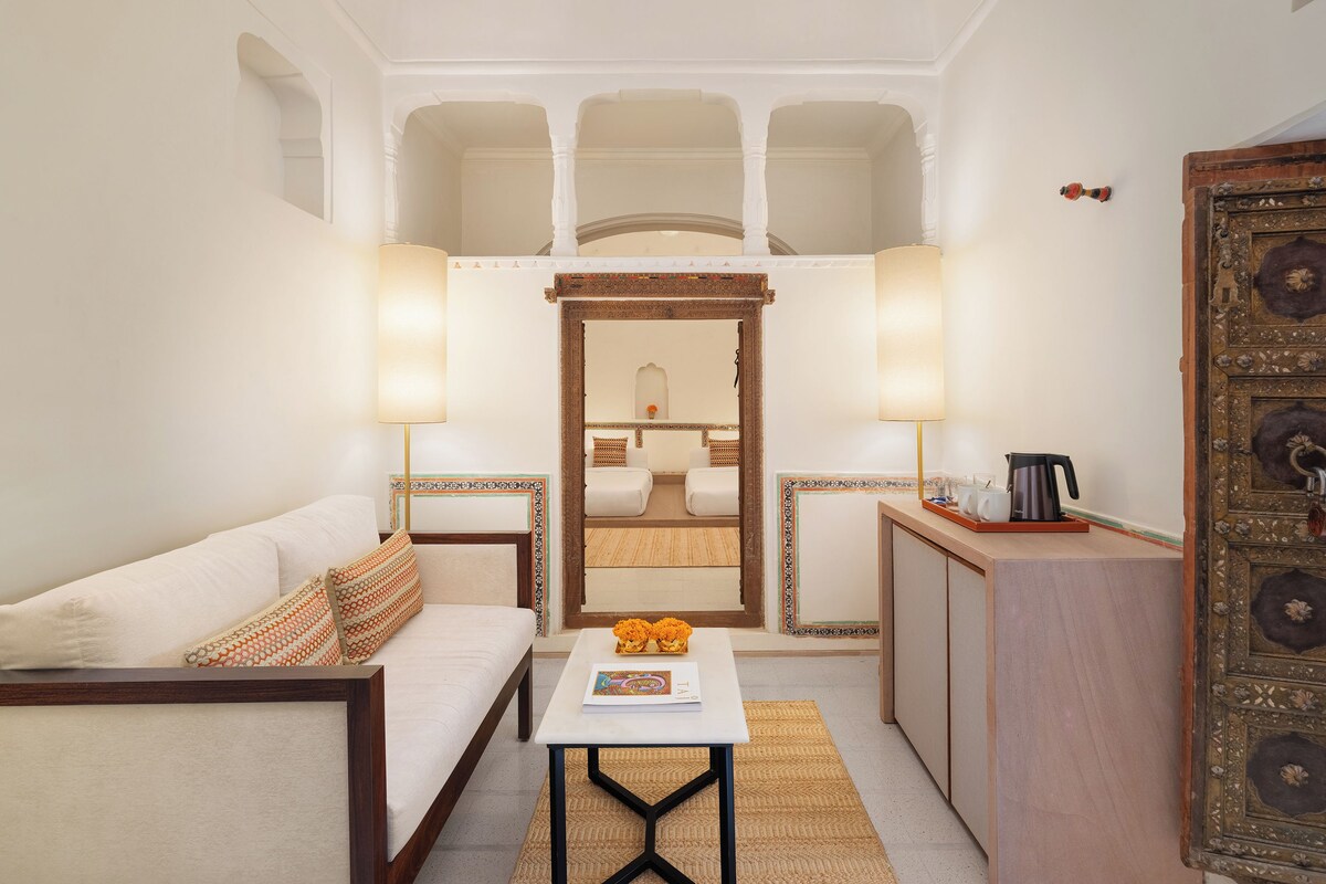 Une chambre d’hôtel compacte comprenant un canapé, une petite table avec un magazine, une machine à café et un meuble décoratif.