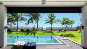 A pool area with a view of the sea, palm trees, and a wooden deck with bean bags. - Ceu Ceylon, Tangalle (Kalametiya)