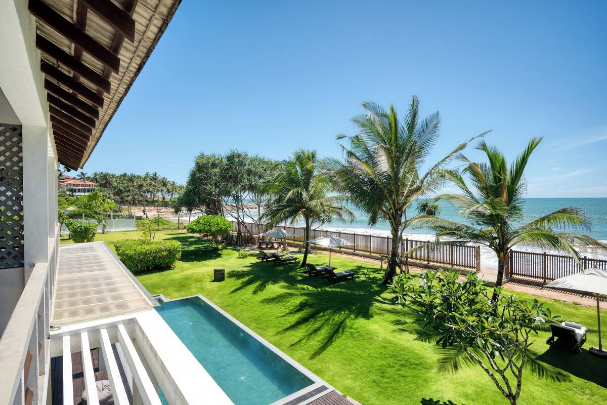 A poolside view with a clear blue sky, palm trees, and a view of the ocean.