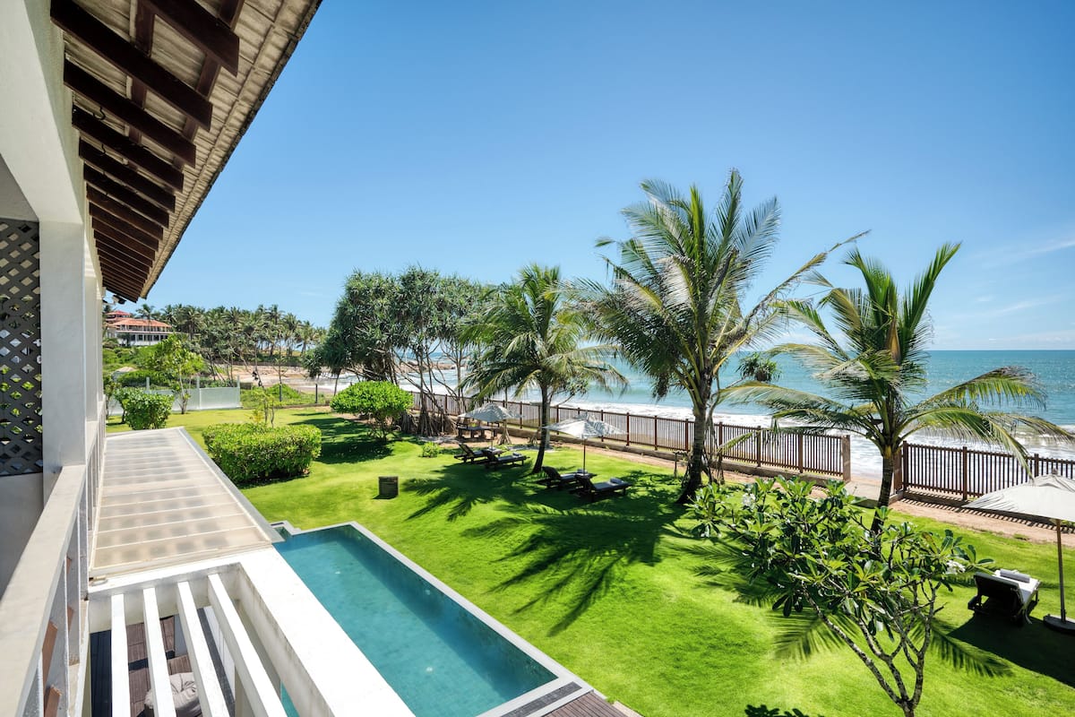 A poolside view with a clear blue sky, palm trees, and a beach in the background.
