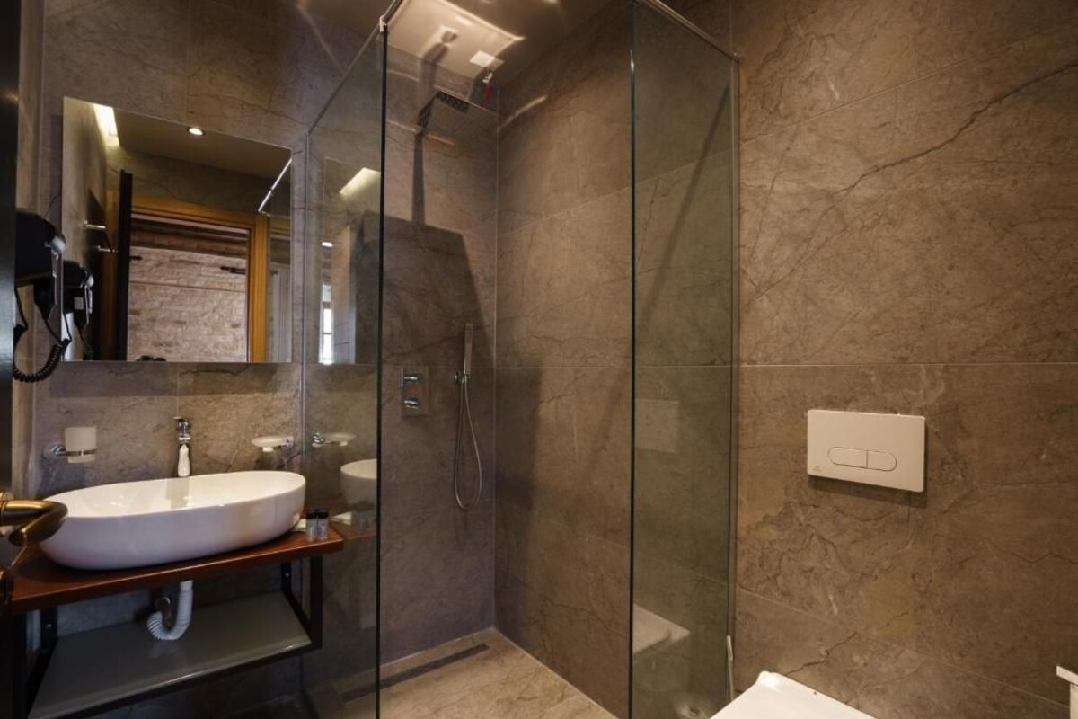 A modern bathroom with a glass-enclosed shower, a freestanding sink, and a marble-tiled wall.