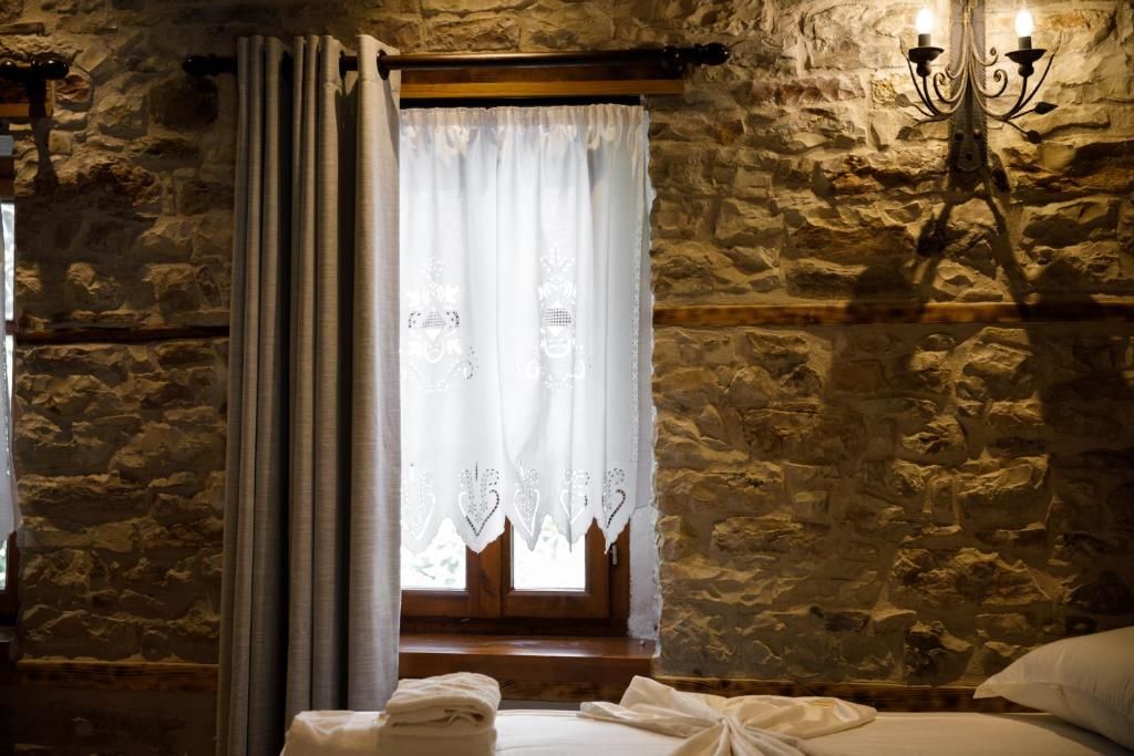 A stone-walled room with a bed, a window with curtains, and a wall-mounted light fixture.