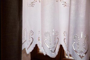 A window with a white curtain featuring intricate cut-out patterns. - Furra Hotel (Gjirokastër)