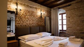 A room with a stone wall, a bed with white linens, a wooden headboard, and a mirror on the left.