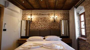 Ein Hotelzimmer mit Steinwand, Holzbalkendecke, einem Bett mit weißen Leinentüchern und zwei Wandlampen.