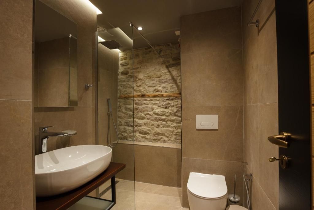 A modern bathroom with a large white sink, a glass-enclosed shower, and a stone accent wall.