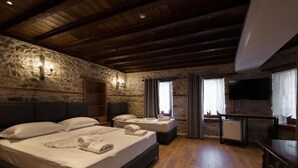 A room with a stone wall, wooden ceiling beams, a bed with pillows and towels, a small table, and a television. - Furra Hotel (Gjirokastër)