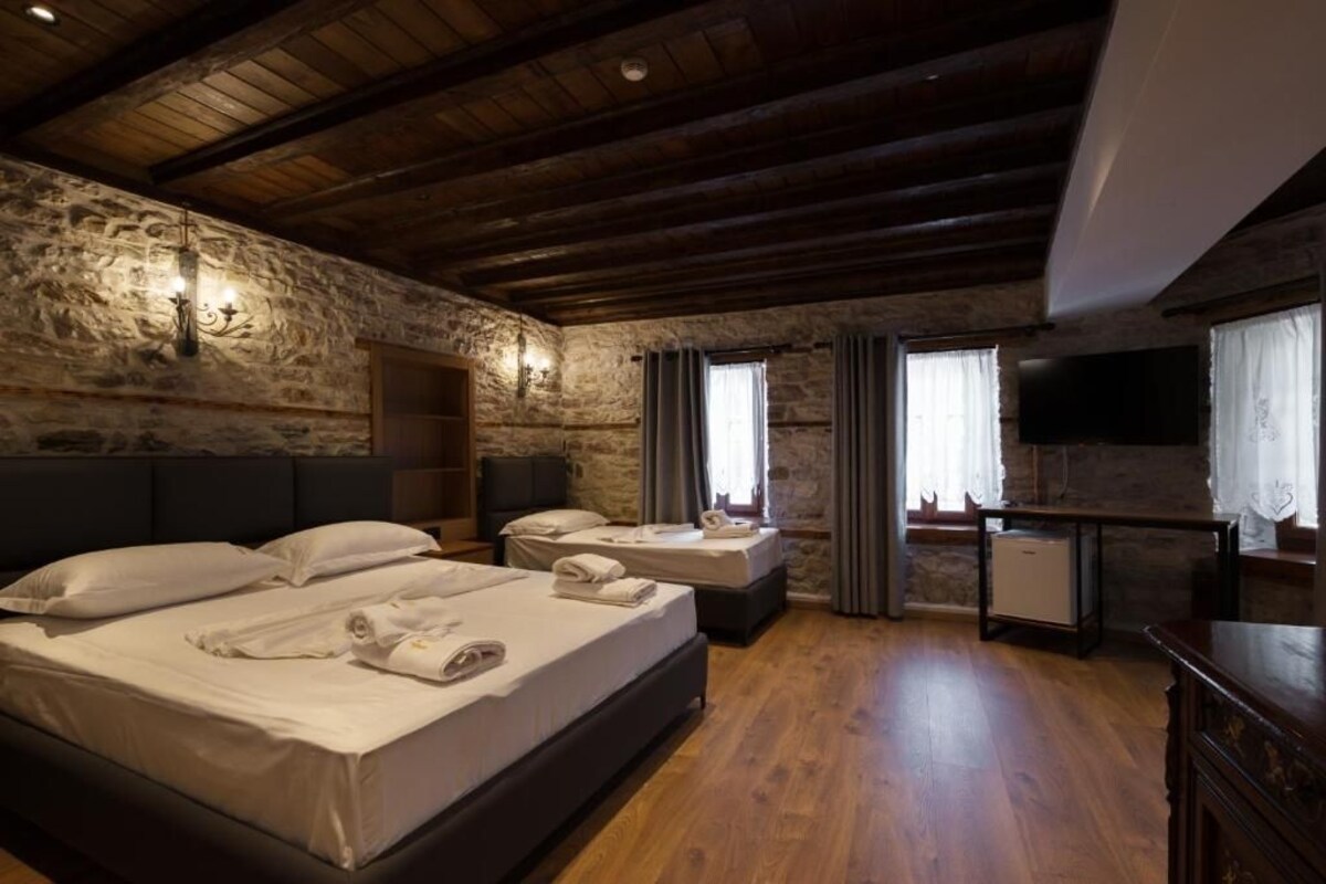A room with a stone wall, wooden ceiling beams, a bed with pillows and towels, a small table, and a television.