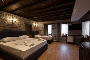 A room with a stone wall, wooden ceiling beams, a bed with pillows and towels, a small table, and a television. - Furra Hotel (Gjirokastër)