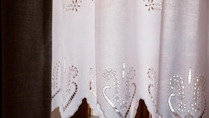 A window with a white curtain featuring intricate cut-out patterns. - Furra Hotel (Gjirokastër)