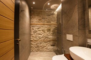 Une salle de bain avec un mur de douche en pierre, une porte en bois et une baignoire blanche.