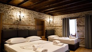 A room with two beds, stone walls, wooden beams, and a window with curtains. - Furra Hotel (Gjirokastër)
