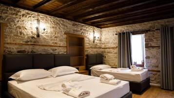 A room with two beds, stone walls, wooden beams, and a window with curtains.