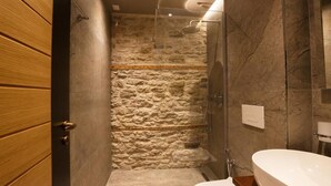 A bathroom with a stone shower wall, a wooden door, and a white bathtub. - Furra Hotel (Gjirokastër)