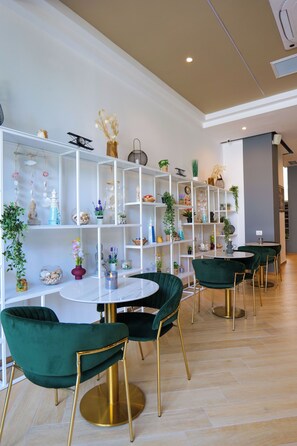 A modern interior with white shelving units filled with decorative items, green velvet chairs, and a round table. - 6 Miles Hotel (Ksamil)