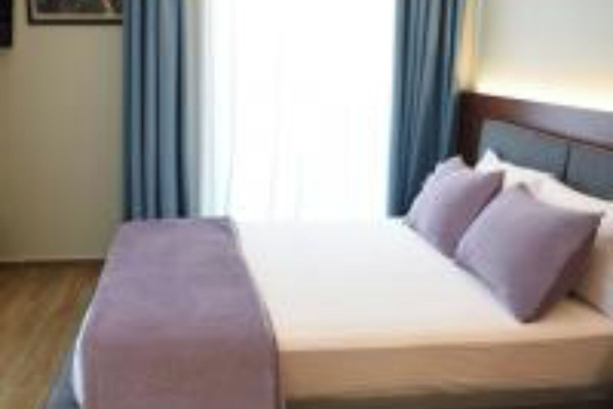 A hotel room with a bed, a bedside table, and a window with curtains.