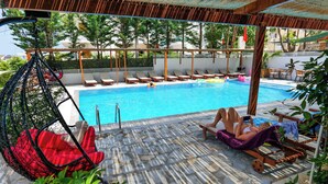 A poolside area with lounge chairs, a swing chair, and a covered seating area.
