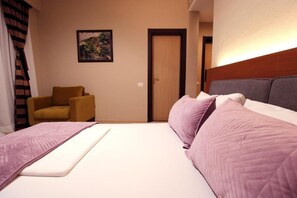 A hotel room with a bed, a chair, a door, and a painting on the wall. - 6 Miles Hotel (Ksamil)