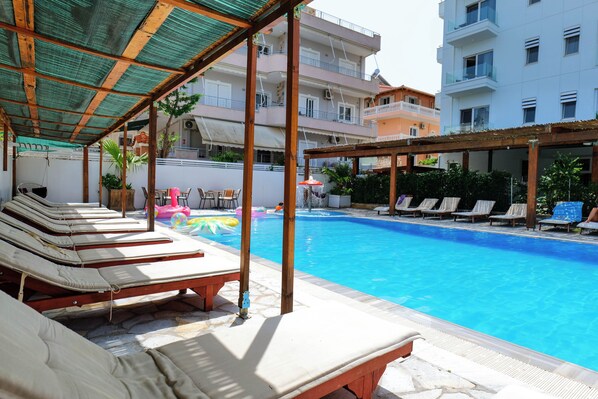 Zona de piscina con sillones de descanso y un área de estar cubierta.