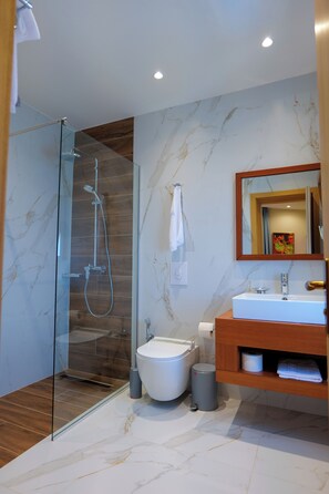 A modern bathroom with a glass-enclosed shower, a white sink, and a wooden vanity. - 6 Miles Hotel (Ksamil)