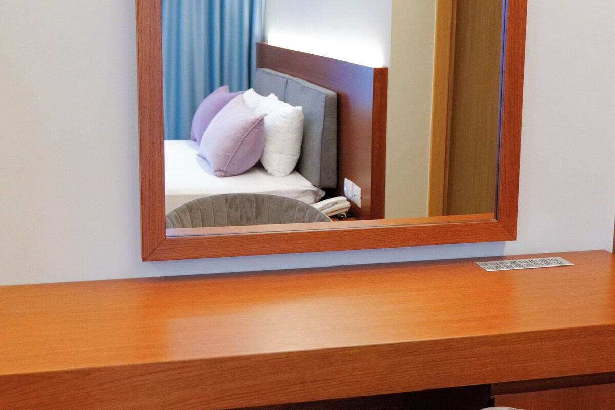 Una habitación de hotel con un escritorio de madera, una silla, una cama con almohadas y un espejo grande.