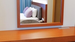 Una habitación de hotel con un escritorio de madera, una silla, una cama con almohadas y un espejo grande.