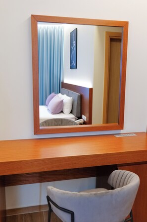 Una habitación de hotel con un escritorio de madera, una silla, una cama con almohadas y un espejo grande.