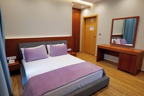 A hotel room with a bed, a desk, a mirror, and a door.