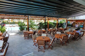 An outdoor cafe with round tables and chairs, a pool in the background, and a bar area. - 6 Miles Hotel (Ksamil)