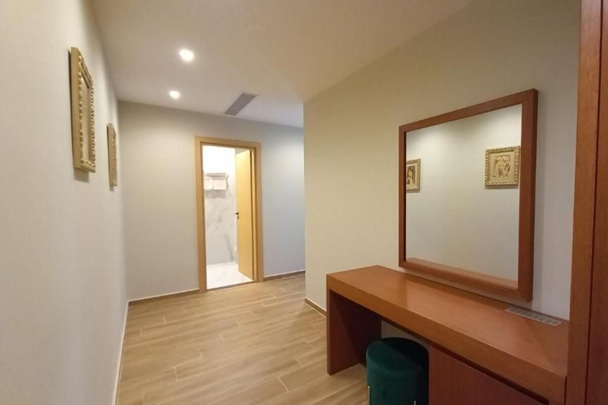 A hallway with a wooden bench, a mirror, and a trash bin.
