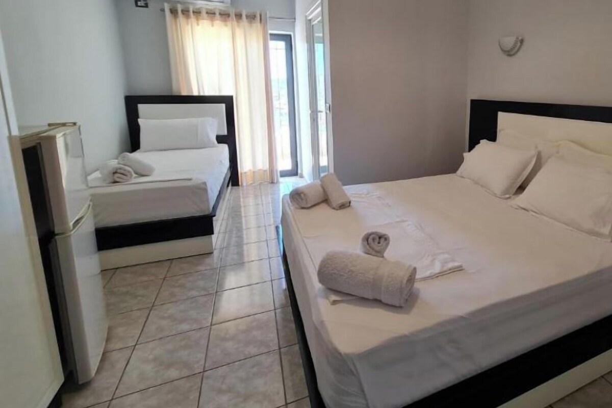 Une chambre d’hôtel avec un grand lit, un lit plus petit, un bureau et une fenêtre avec des rideaux.