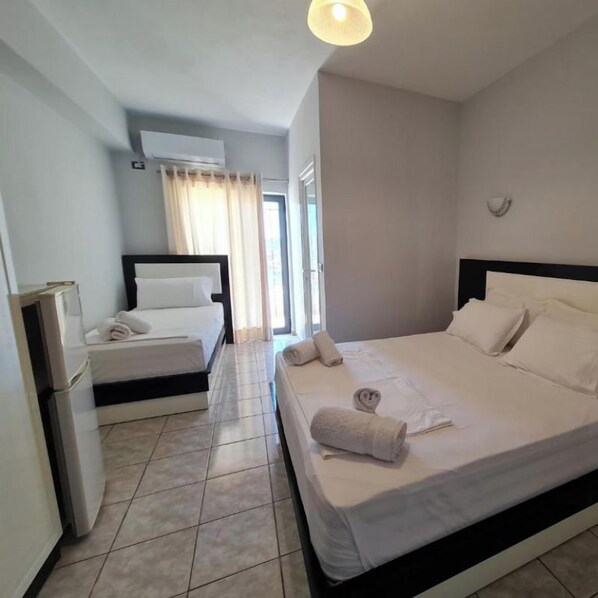 Une chambre d’hôtel avec un grand lit, un lit plus petit, un bureau et une fenêtre avec des rideaux.