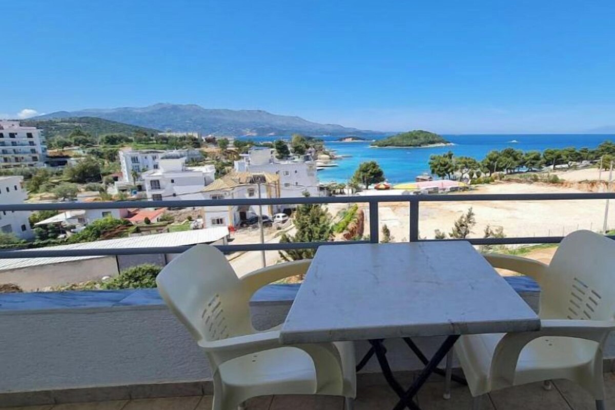 Un balcon avec une table et des chaises donnant sur une vue côtière, avec des bâtiments et une plage.