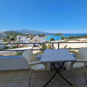 Un balcon avec une table et des chaises donnant sur une vue côtière, avec des bâtiments et une plage.