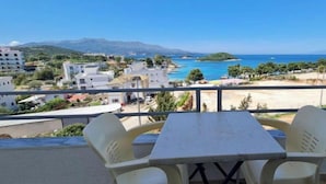 Un balcon avec une table et des chaises donnant sur une vue côtière, avec des bâtiments et une plage.